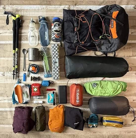 Complete backpacking gear layout with pack, trekking poles, tent and sleeping bag