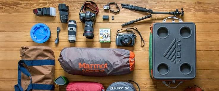 Camera and camping gear flat lay: DSLR camera, lenses, flash, instant camera, tripod, packed tent, duffel bag and a rugged cooler