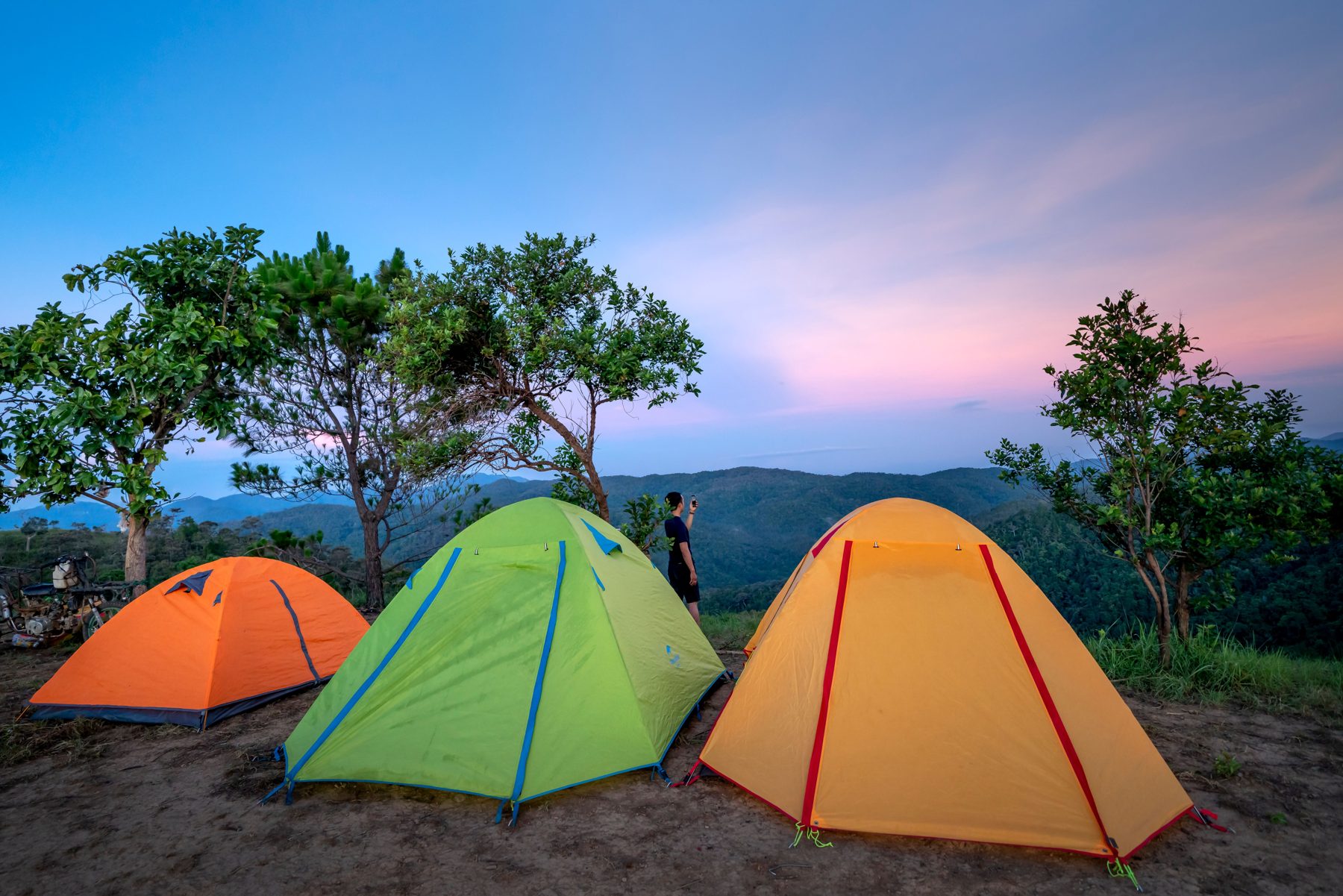 Orange, green and yellow dome tents on a mountain clearing at dusk