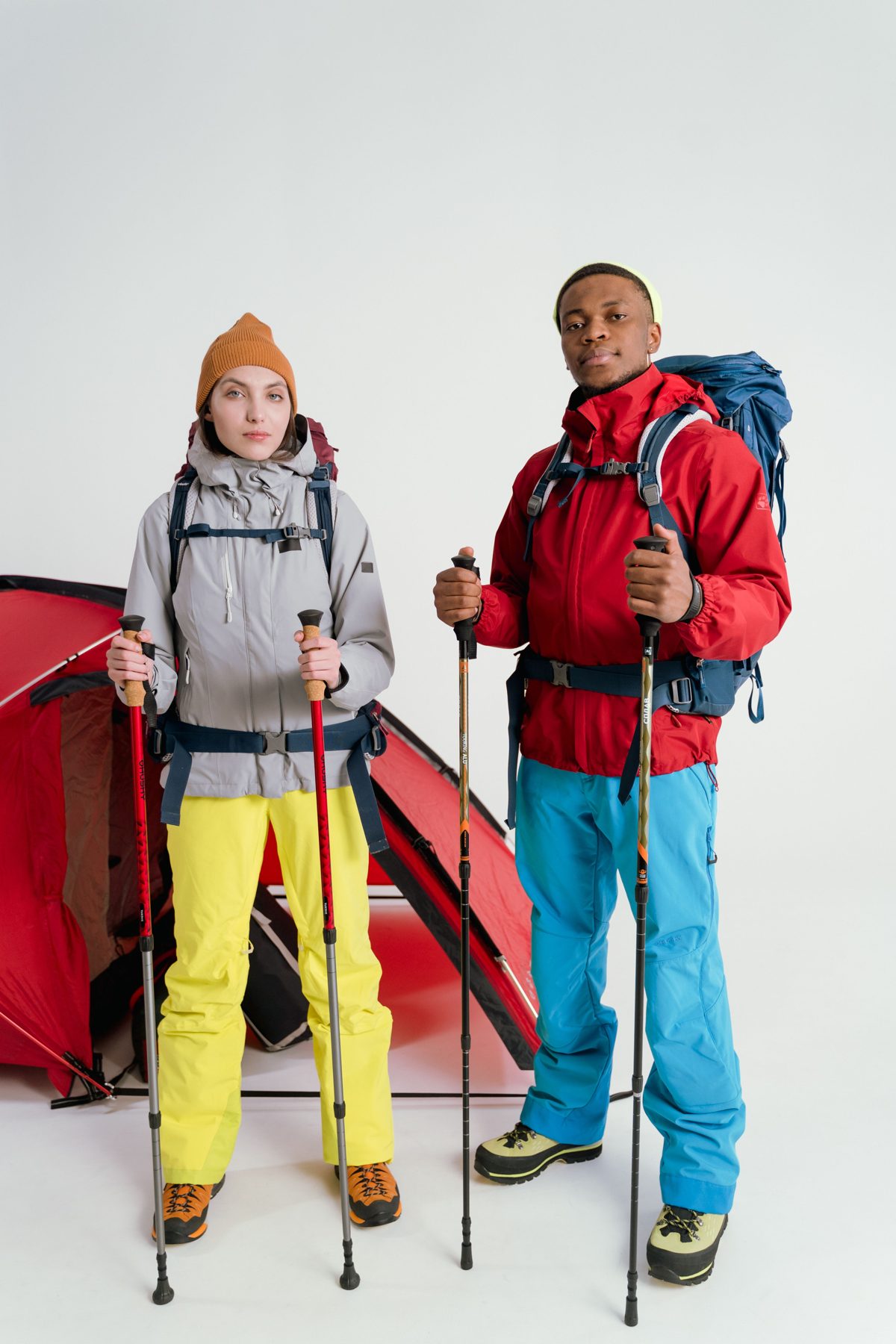 Two hikers with backpacks, rain jackets and trekking poles standing in front of a red tent